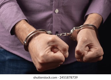 Businessman in handcuffs arrested for financial fraud, sitting in interrogation room.