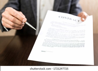 Businessman handing over a contract for signature offering a ballpoint pen in his hand