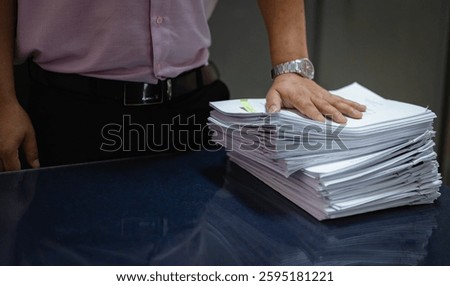 Businessman handling a large stack of documents in an office. Concept of paperwork overload, business administration, and corporate workload. Professional hands managing report and contract on a desk.