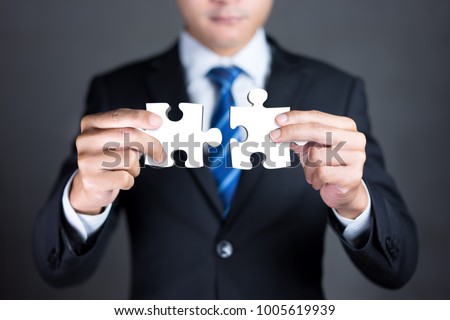 Businessman hands connecting puzzle pieces representing the merging of two companies or joint venture, partnership, Mergers and acquisition concept.