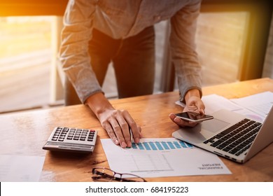 Businessman Hands Holding Pen And Smartphone Mobile With Calculator Laptop Computer And Graph Chart For Calling Analytics Consultant Marketing Department With Partner.