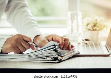 Handbuecher für Geschäftsleute, die Stift für die Arbeit in Papierstapeln für die Suche nach Informationen Business-Report-Papiere und Haufen unfertiger Dokumente auf Laptop-Computer in modernen Büros