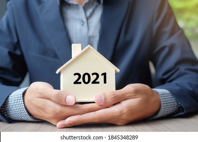 Businessman hands holding wooden House model with 2021 New Year text. Property insurance and real estate concepts