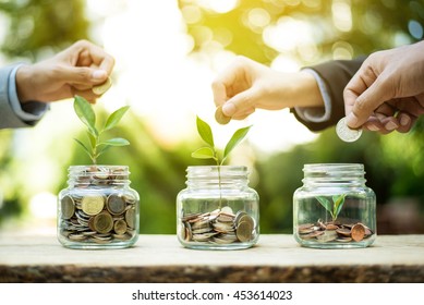 Businessman hands putting money (coin) into the glass jar - savings and investment  concept