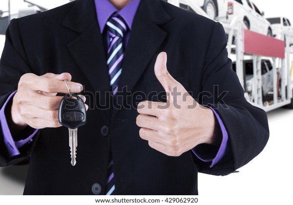 Businessman hands showing a car key and thumb\
up with trailer truck\
background