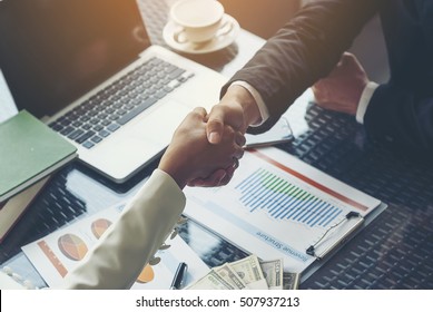 Businessman handshaking for business cooperation, Chart documents showing income structure and a laptop, along with a large number of banknotes placed on the table for signing commercial contracts. - Shutterstock ID 507937213