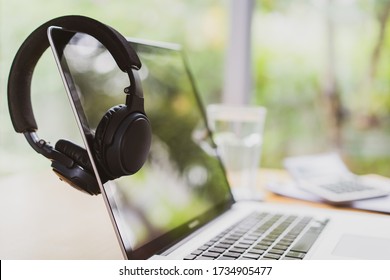 Businessman hanging his modern wireless headphones over the laptop computer screen while taking a break. Setting up working space or home office. Work from home concept with copy space for background.