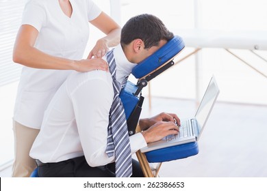 Businessman having back massage while using laptop in medical office