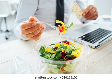 Businessman having a lunch break at desk, he is eating fresh salad and holding a cracker, unrecognizable person - Powered by Shutterstock