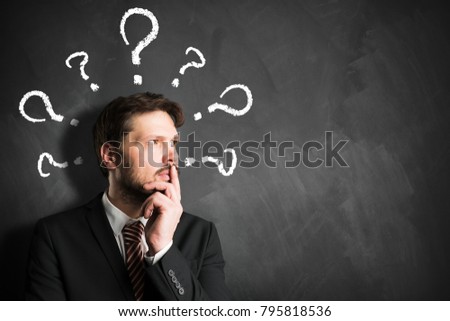 businessman having many questions symbolized as questionmarks on a blackboard over his head