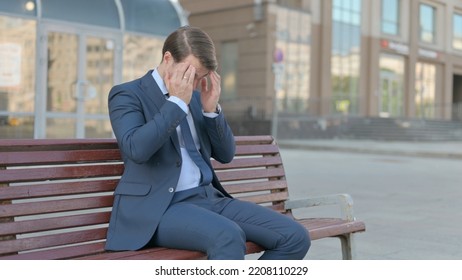 Businessman With Headache Sitting Outdoor On Bench