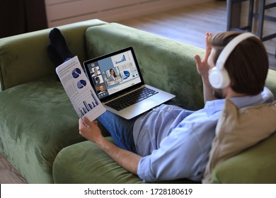 Businessman in headphones lying on sofa talking to her colleagues in video conference. Multiethnic business team working from home using laptop, discussing financial report of their company. - Shutterstock ID 1728180619