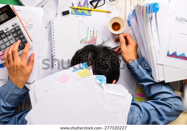 Businessman heavy\
workload sleep at office desk with finance sheet calculator and\
coffee.(concept for\
overworked)