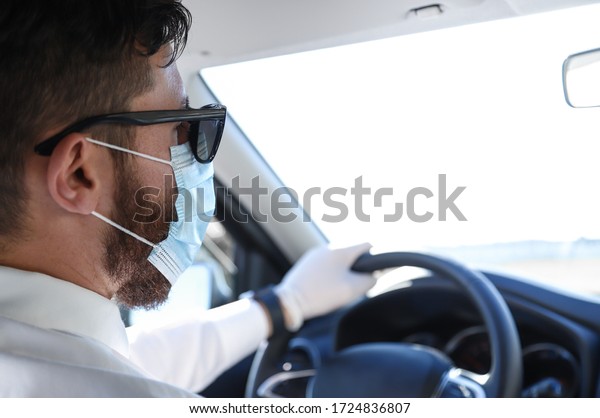 \
Businessman with hipster look drives his\
car wearing mask and gloves to prevent coronavirus. Excellent photo\
to express the concept of\
responsibility