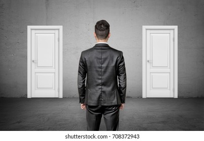 A businessman with his back turned stands between two identical closed white doors. Make right choice. Important decision. Never fail. - Powered by Shutterstock