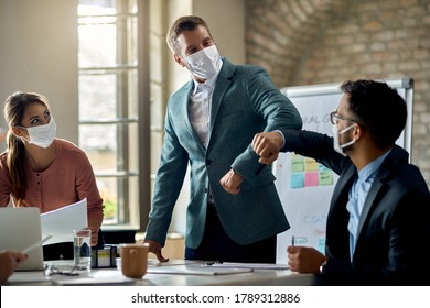 Businessman and his coworker wearing protective face masks and elbow bumping while greeting in the office. - Powered by Shutterstock