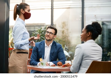 Businessman and his female colleague talking to waitress who is wearing proactive face mask in a restaurant. 