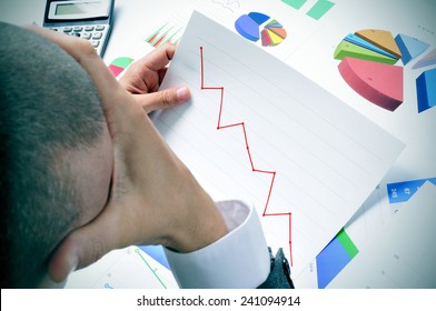 Businessman In His Office Desk Full Of Graphs And Charts Observing Worried A Chart With A Downward Trend