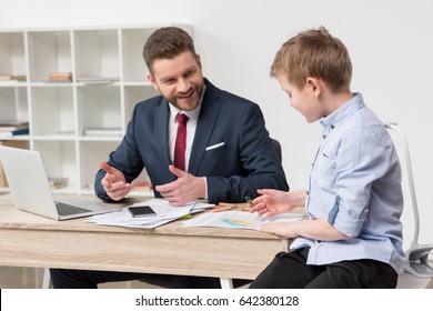 Businessman with his son drawing on business papers at office - Powered by Shutterstock