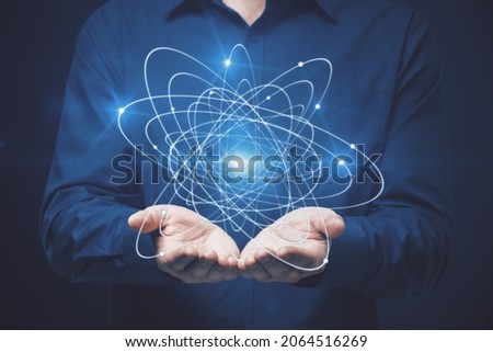 Businessman holding atom on dark background. Science concept