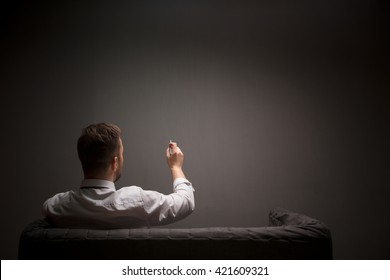 Businessman Holding Ballpen In Front Of Him While Sitting On Comfortable Sofa In Studio. Back View Of Young Man Writing Something.