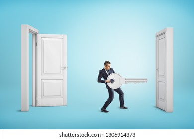 Businessman Holding Big Key Between An Open Door And A Closed One On Blue Background. Business And Management. Way To Success. Taking Chances.