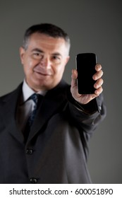 Businessman Holding Up A Blank Mobile Phone Extended Towards The Camera With Focus To The Phone