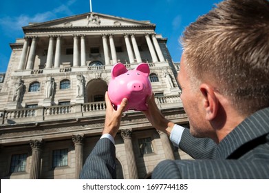 Businessman holding a bright pink piggy bank outside the traditional architecture of the Bank of England in the City financial center of London, UK