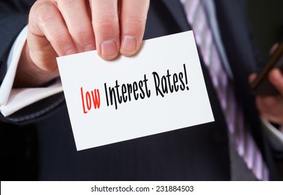A businessman holding a business card with the words, Low Interest Rates, written on it.