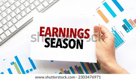 Businessman holding a card with text EARNINGS SEASON .Keyboard, diagram and white background