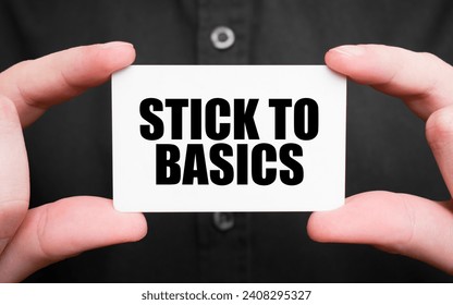 Businessman holding a card with text STICK TO BASICS, business concept