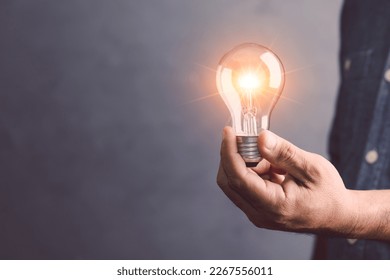 Businessman holding a clear light bulb with light effect on gray space wall background. Concept of new ideas for work. - Powered by Shutterstock