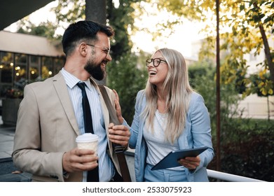 Businessman holding a coffee and a businesswoman holding a tablet are walking and laughing together on a break outside the office - Powered by Shutterstock