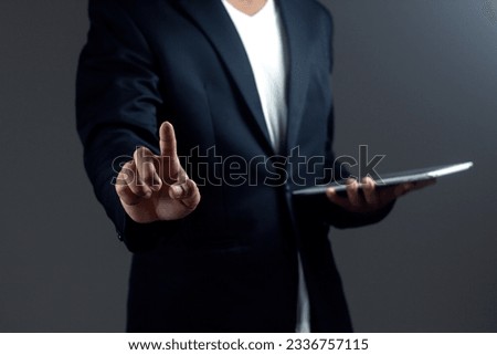 Businessman is holding digital tablet and pointing index finger against background. 