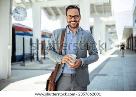 Businessman holding a disposable coffee cup at the train station platform. A man in a train station commuting to work. Businessman with coffee cup. Man waiting for train and drinking coffee.