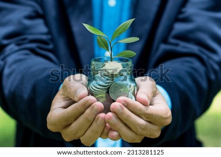 Businessman holding glass jar with small plant and coin inside. Financial and business background.Investing growth, growing business concept.