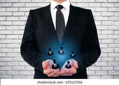 Businessman holding glowing HR hologram on brick wall background. Hiring concept 