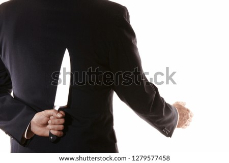 Businessman holding a knife behind his back is about to shake hands. This is to signify someone who is a traitor and not to be trusted about to stab you. Copy space.