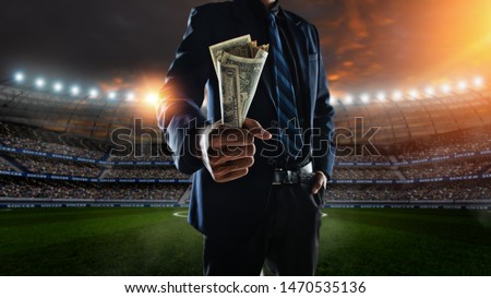 businessman holding large amount of bills at Soccer stadium in background