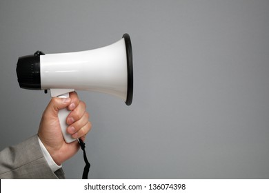 Businessman holding a megaphone in front of blank gray background ready for message - Powered by Shutterstock