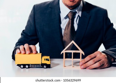 Businessman Holding A Miniature Of House And Delivery Toy Truck, Indicating The Concept Of Direct Delivery To House, Moving Relocation And Freight Service.