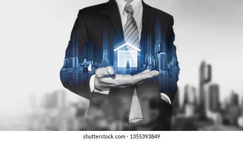 Businessman holding modern buildings hologram, and home icon. Real estate business, building technology and smart home concept