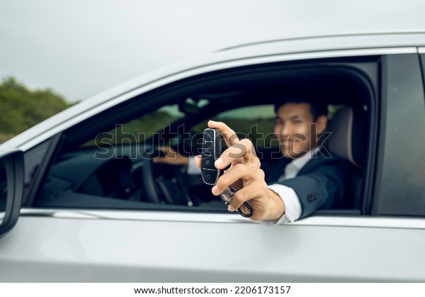 Businessman\
holding modern car keys, alarm system and steering wheel with\
electric buttons - male hand holding\
keys