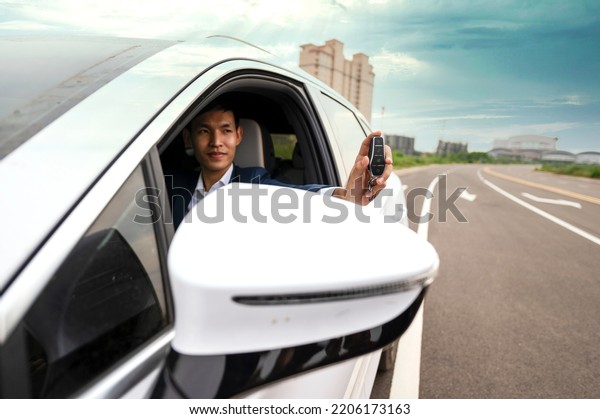Businessman\
holding modern car keys, alarm system and steering wheel with\
electric buttons - male hand holding\
keys