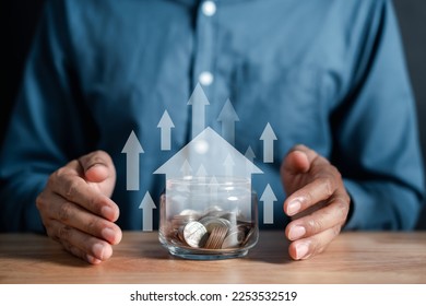 Businessman holding a money jar with a house inside to make a profit on interest real estate investment growth value, home interest rate, inflation, planning future inflation and passive income. - Shutterstock ID 2253532519