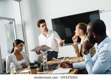 Businessman Holding Newspaper Near Thoughtful Business Partners In Conference Room