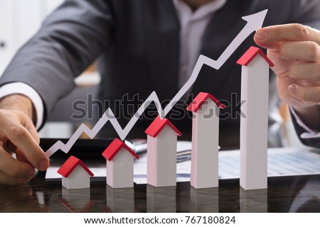 Businessman Holding Paper Graph Over The Increasing House Miniature