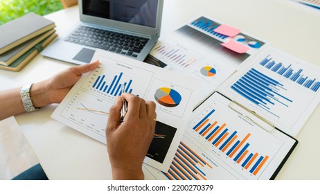 Businessman Holding Pen And Pie Chart Document Showing Company Financial Data He Sits In A Private Office With A Laptop Analyzing Financial Data In Chart Form. Financial Concept