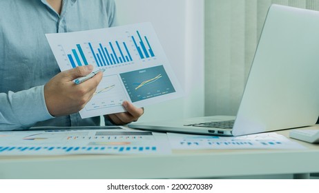 Businessman Holding Pen And Pie Chart Document Showing Company Financial Data He Sits In A Private Office With A Laptop Analyzing Financial Data In Chart Form. Financial Concept