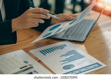 Businessman Holding Pen And Pie Chart Document Showing Company Financial Data He Sits In A Private Office With A Laptop Analyzing Financial Data In Chart Form. Financial Concept